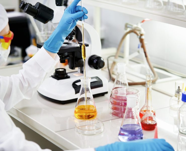 Science, chemistry, technology, biology and people concept - young female scientist mixing reagents from glass flasks and making test or research in clinical laboratory